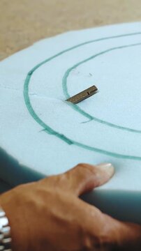 Vertical video. Close-up of a worker's hands cutting paralon with a power tool for sofa production at a furniture factory, slow motion.