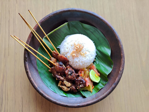 Traditional Indonesian satay with rice, sambal, and lime served on banana leaf in wooden bowl.