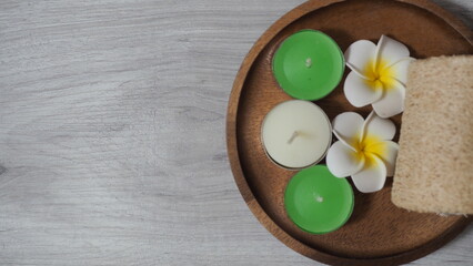 White rolled bath towel with eucalyptus branch, black massage stone and candle on clean marble table for a relaxing spa experience.