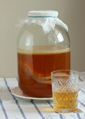 Homemade kombucha fermenting in glass jar with a glass of kombucha tea