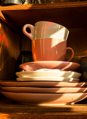 Stacked pink and white coffee cups and saucers illuminated by warm sunlight