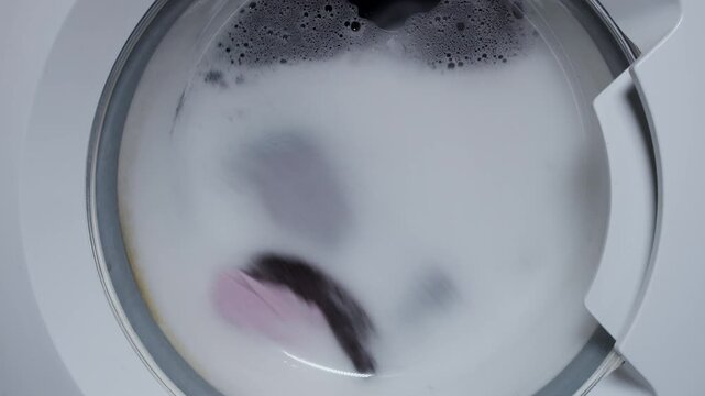 Close up video of spinning washing machine drum with foam spraying door, Washing clothing in domestic washing machine