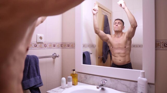 Muscular man dancing and flexing in bathroom mirror