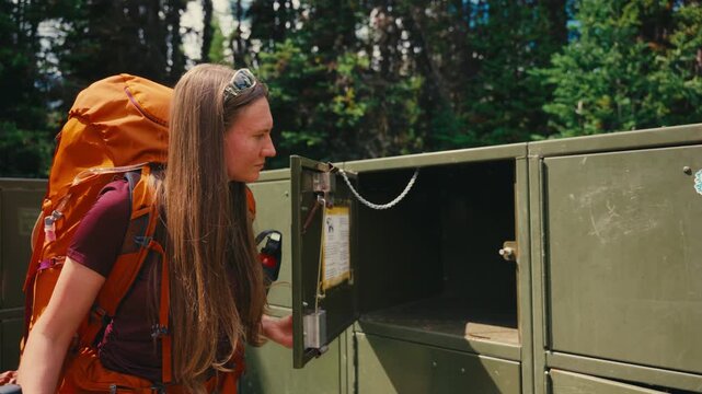 Female backpacker using bear proof food storage container in forest, Canadian Rockies