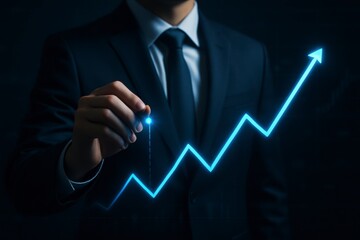 Businessman in suit drawing a bright blue upward trending graph with a glowing pen on a dark background