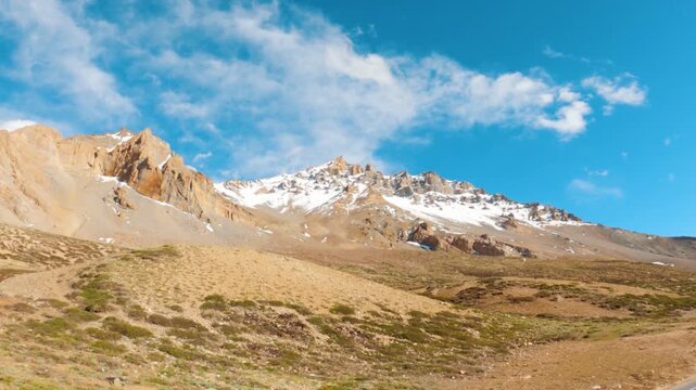 Landscape shot of snowy Himalayan mountain peaks with clouds against the blue sky as seen from Sarchu in Leh Manali Highway, India. Scenic view of dry mountain peaks with snow on top at Ladakh.