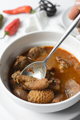 Overhead view of Nigerian goat pepper soup in a white soup plate, top view of goat meat pepper soup in a plate, traditional goat peppersoup in a white bowl