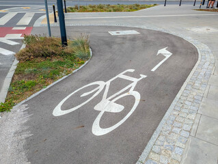 Obraz premium Curved bicycle path with white painted cycling symbol on dark asphalt creating smooth transportation route. High quality photograph