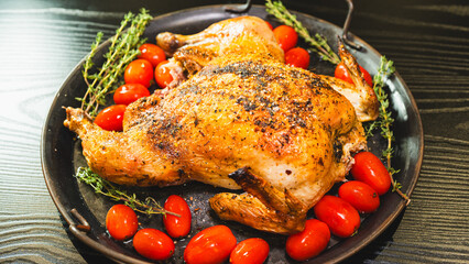 Golden brown whole roast chicken with fresh thyme and cherry tomatoes on a rustic wooden board. Top view, beautifully presented for food blogs and advertising.