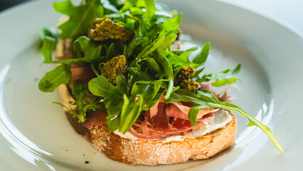 Beautifully served toast with fresh mozzarella, authentic Italian prosciutto, vibrant arugula and green pesto sauce. Perfect for food blogs and menus.