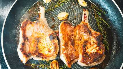 Juicy bone-in pork chops sizzling in a pan with golden fried garlic and fresh thyme sprigs....