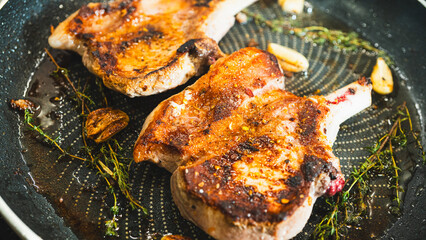 Juicy bone-in pork chops sizzling in a pan with golden fried garlic and fresh thyme sprigs....