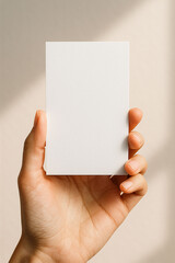 Closeup of hand holding a blank card in soft light, minimalist background
