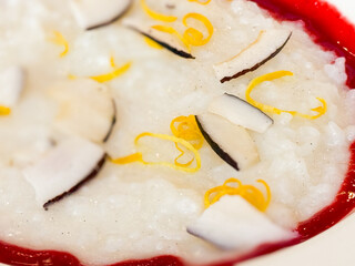 Close-up white porridge with coconut, lemon zest, and berry sauce served in a plate. Breakfast, nutrition and balanced healthy eating with hot drink.