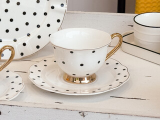 White ceramic cup with golden handle and black polka dots on saucer. Home decor, kitchenware, and stylish tableware design.