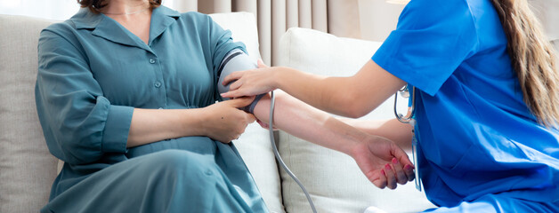 Obraz premium Caregiver caucasian young nurse woman measuring blood pressure with patient for checkup pulse health and examining in living room at home, nurse checkup patient for health care, medical and insurance.