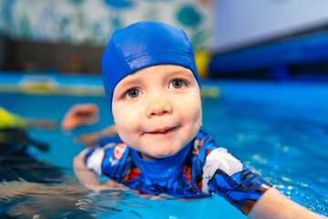 Young child enjoys swimming in pool. A smiling child wearing a blue swim cap practices swimming in a colorful indoor pool during a lesson.