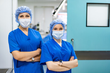 Surgical-clad healthcare staff. Two healthcare workers wear scrubs and masks, standing confidently in a medical facility, ready for their duties.