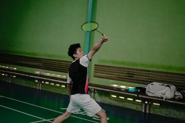 A determined badminton player using backhand style at an indoor sports facility