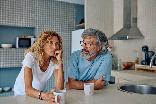 Senior couple sharing breakfast in their modern kitchen, discussing their worries and challenges while sipping coffee and tea together