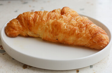 Plate with one fresh croissant on white marble  table