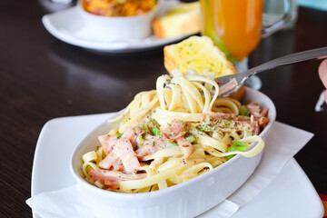 Delicious creamy pasta fettuccine served with ham, herbs, and vegetables in a white bowl. Italian cuisine comfort food close-up, perfect for restaurant menu, recipe, or culinary concept.