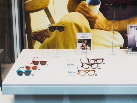 Displaying various eyeglasses models from luxury brands like Gucci and Versace in a shop window with lifestyle promotions