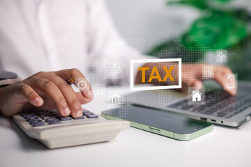 Obraz premium A person calculating taxes with a calculator and laptop, featuring a holographic display of financial icons and the word TAX, representing financial management, accounting, and online tax services.