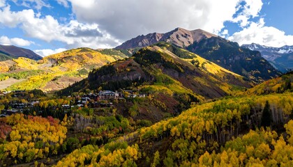 A vibrant autumn landscape showcasing a mountain valley with colorful aspen trees, a picturesque village nestled amidst the hills, and a backdrop of towering peaks under a partly cloudy sky.