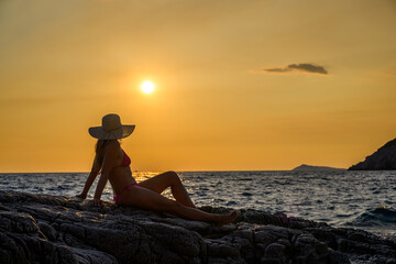 Brunette in pink bikini with straw hat at seaside during sunset in Montenegro