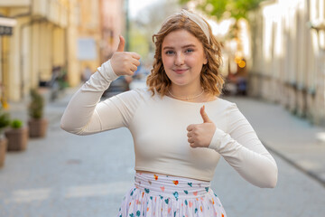 Like. Happy red hair woman raises thumbs up agrees with something or gives positive reply recommends advertisement likes good idea feedback celebrating success victory outdoors. Girl in city street.