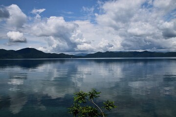 Scenic view of Lake Tazawa in Akita, Japan, with mountains and dramatic clouds reflecting on the calm, mirror-like water surface.
