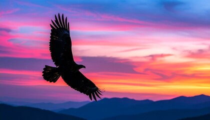 Majestic eagle soars through a vibrant sunset sky above a mountain range.