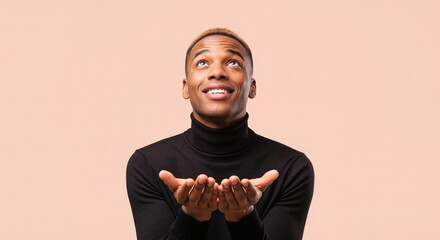 Hopeful young African American man in a black turtleneck looking up with cupped hands, praying or receiving a blessing