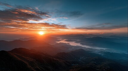 A breathtaking sunrise paints the mountain peaks with fiery hues, showcasing a serene vista of valleys and distant lakes nestled amongst the towering ranges.
