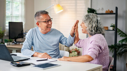 Cheerful Asian Senior Couple High Fiving at Home Office Celebrating Success Retirement Planning Happy Lifestyle Together