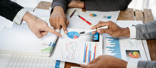 Three people are looking at a table with a lot of papers and graphs
