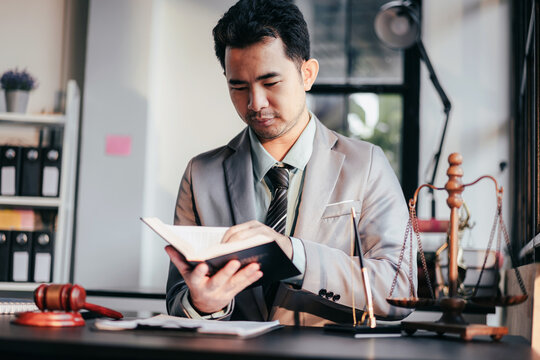 Asian Lawyer Reading Law Book at Office Desk with Gavel and Scale of Justice Legal Research Attorney Law Firm and Legal Representation Concept