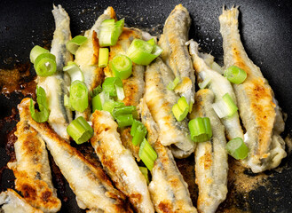 Fried smelt fish in a pan with green onions