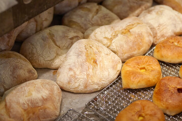 Assorted bakery bread loaves and buns displayed on a tray, featuring rustic flour-dusted bread and golden rolls