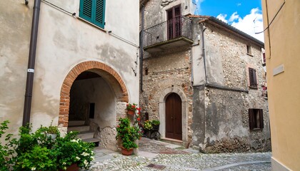 A narrow alleyway winds through a picturesque Italian village, showcasing aged stone buildings and vibrant flowers.