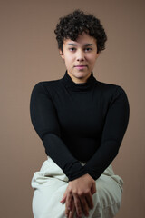 Beautiful young woman with no make up, sitting with crossed legs and hands on knee. Perfect for Generation Z attitude, self-confidence, femininity and individuality. Studio portrait, copy space.