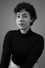 Black and white portrait of young woman with short curly hair and blank expression. Ideal for Gen Z identity, femininity and individuality concepts.