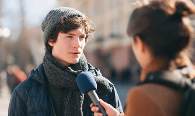 A person being interviewed on the street with a microphone, wearing a beanie and scarf. © Artlana