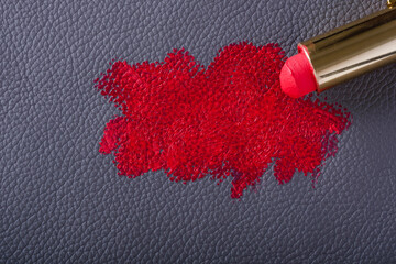 A vibrant red lipstick is being swatched on a smooth blue leather surface, highlighting the rich color and texture of both the makeup and the material beneath.