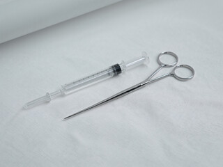 Medical syringe with clear liquid and surgical forceps on white fabric health healthcare