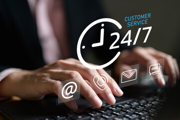 Professional hands typing on laptop with 24/7 customer service interface showing clock icon and communication symbols including email, phone and chat. Round-the-clock support service concept.