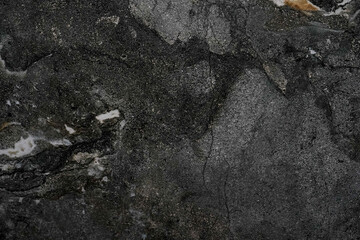 A close-up of a dark rough stone surface with natural cracks and mineral patterns