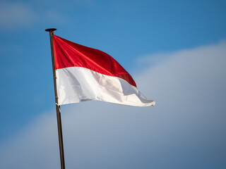 The Indonesian red and white flag flutters proudly in the wind against a bright blue sky.