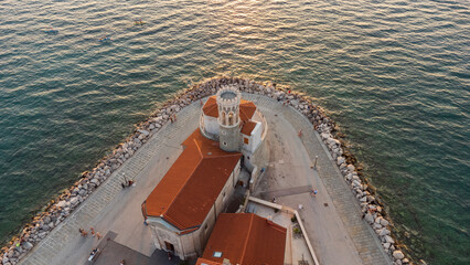View from above of Our Lady of Health Church in Piran, with the tower near sunset and the sea nearby. A tourist attraction at the tip of the Piran peninsula, Slovenia